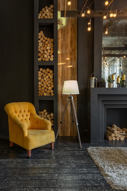 Interior oscuro y brutal de la sala de estar decorada con troncos de madera. sillones suaves amarillos y grises, ventana de arco enorme y chimenea