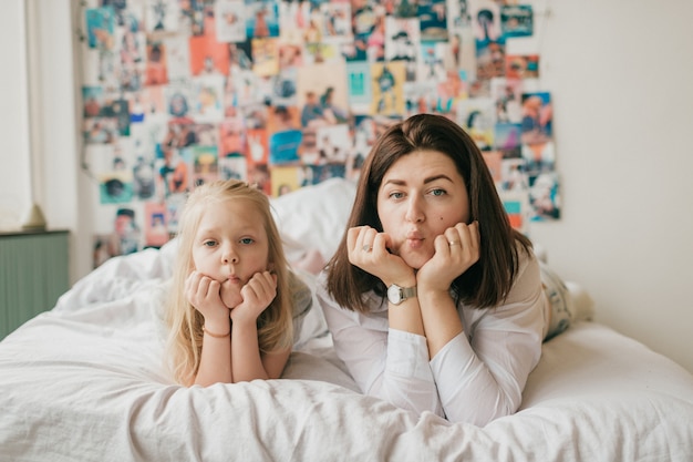 Interior retrato de familia feliz de sonriente madre y su hija acostado juntos en la cama con pared decorativa detrás