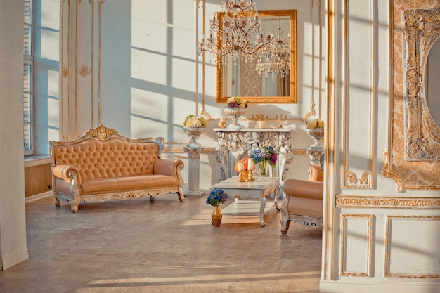 Interior rico do apartamento com decorações barrocas douradas nas paredes e móveis de luxo. a sala está inundada com os raios do sol poente