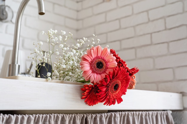 Interior rústico de cozinha branca com flores vermelhas de gérbera fresca dentro da pia