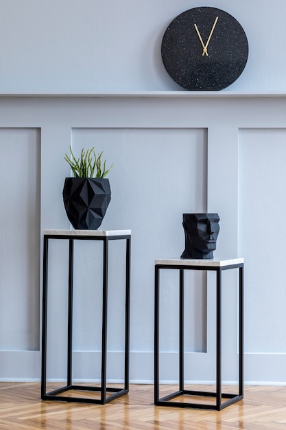 Interior de la sala de estar escandinava con estilo con taburetes de mármol de diseño, plantas, reloj negro en el estante y accesorios elegantes en la decoración minimalista del hogar.