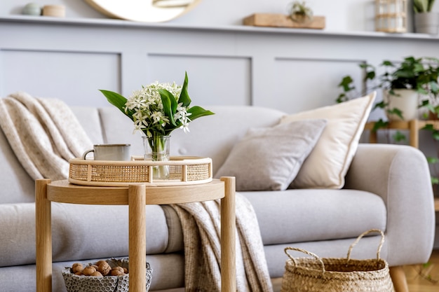 Interior de la sala de estar escandinava con sofá gris de diseño, mesa de centro de madera, plantas, estantería, flores de primavera en florero, decoración y elegantes accesorios personales en la decoración del hogar.