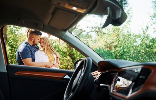 Interior del vehículo. Pareja abrazándose en el bosque cerca de coche moderno.