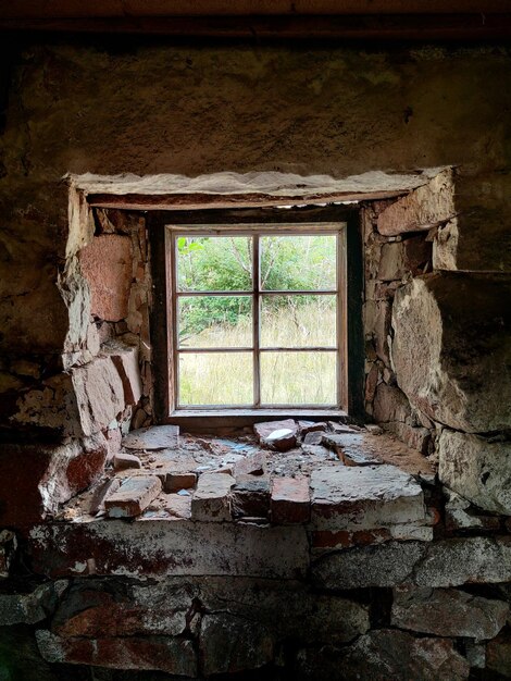 Foto interior de una vieja construcción abandonada con ventana enmarcada en piedra con vista a la naturaleza verde