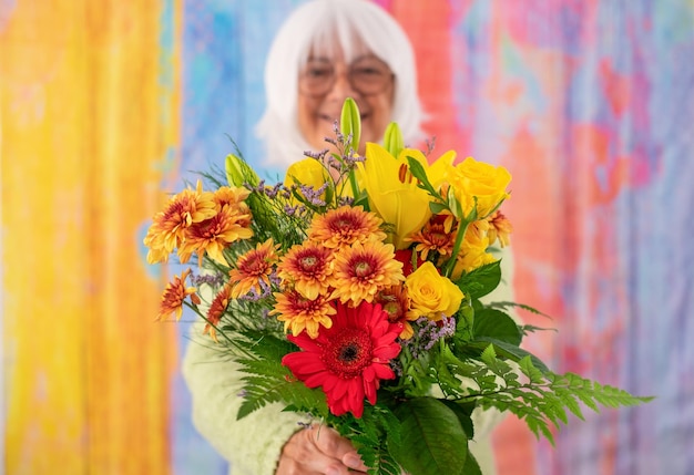 Internationaler Frauentag Verschwommene, glückliche, weißhaarige Seniorin, die einen Strauß Frühlingsblumen hält