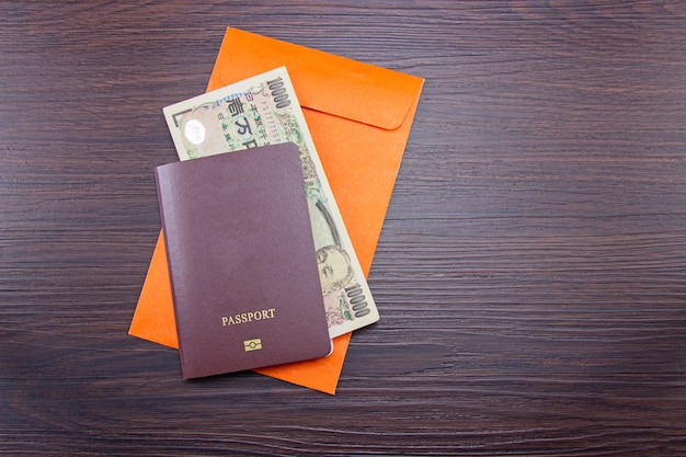 Foto internationaler pass und japanische banknoten auf orangefarbenem umschlag am braunen dunklen holz des tisches.