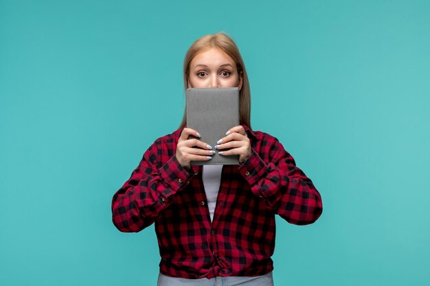 Internationaler Studententag junges süßes Mädchen in rot kariertem Hemd, das das Gesicht mit dem Buch bedeckt