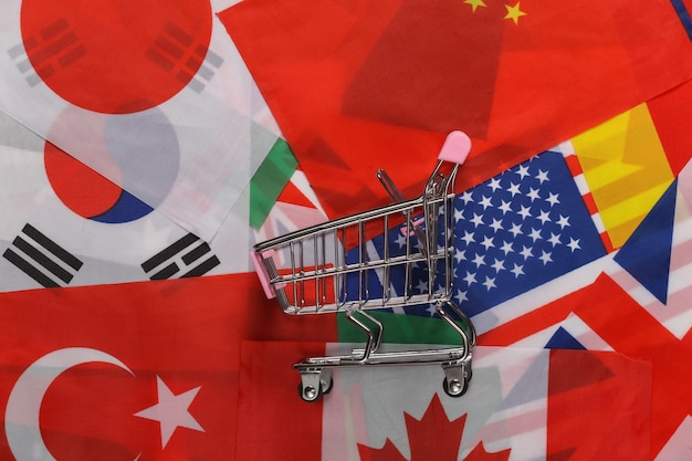 Internationales Einkaufen. Einkaufswagen auf dem Hintergrund vieler Flaggen der Länder