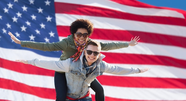 Internationales Freundschafts-, Freiheits- und Menschenkonzept - glückliches Teenager-Paar in Schattierungen, das sich über dem Hintergrund der amerikanischen Flagge amüsiert