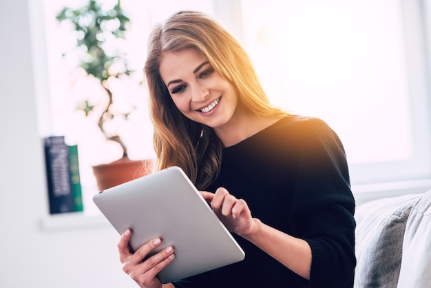 Internet de navegação em casa. Mulher jovem e bonita usando tablet digital com um sorriso enquanto está sentada no sofá em casa