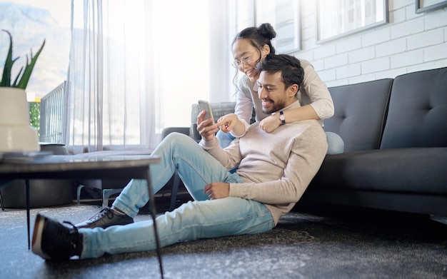Interracial Paar und Menschen mit Telefon in sozialen Medien lachen über Meme oder lustige Internetinhalte Mann, Frau und Liebhaber entspannen sich im Haus oder in der Wohnung beim Surfen auf der Website oder App