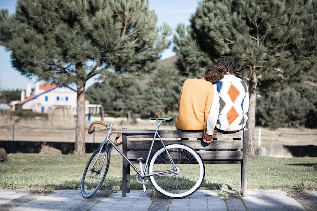 Foto interracial pareja de enamorados cogidos de la mano sentado en un banco en un parque junto a su bicicleta