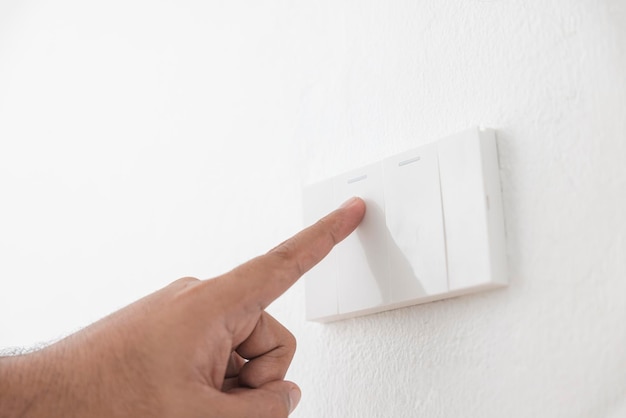 El interruptor de luz de primer plano de un dedo macho encenderá o apagará un interruptor de luz con pared blanca en casa interruptor mecánico de plástico blanco montado Energía energía ahorrar electricidad espacio de copia