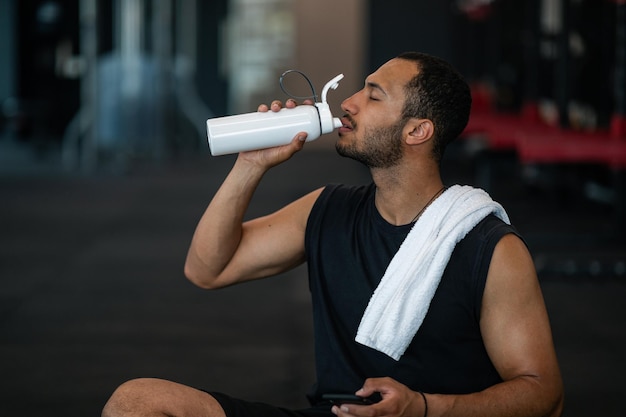 Intervalo de treino desportivo jovem negro bebendo água após o exercício no ginásio