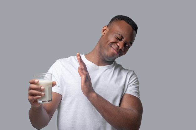 Foto intolerância a lactose. um homem de pele escura em uma roupa branca segurando um copo com leite