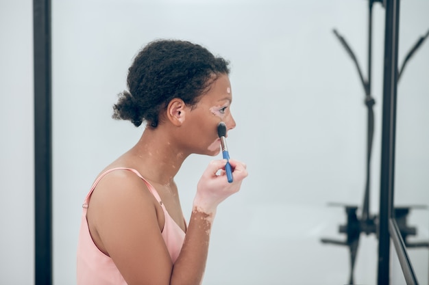 Inventar. Una mujer bonita de pelo rizado haciendo maquillaje y luciendo complacida