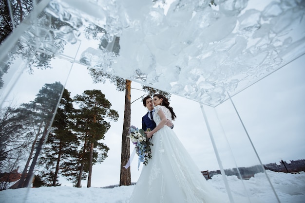 Inverno encenou a fotografia do casamento. Noiva e noivo com um lindo buquê ao lado de uma mesa de vidro e cadeiras