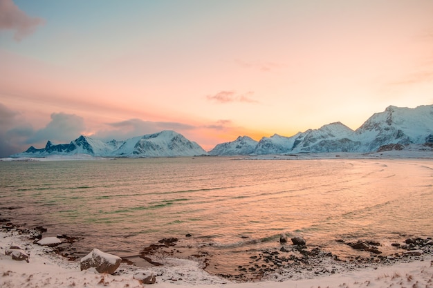 Inverno. fiorde norueguês rodeado por montanhas cobertas de neve no início da manhã. céu rosa do sol nascente refletido na água