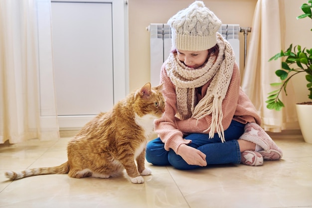 Inverno frio, temporada de outono, menina, aquecendo-se perto do radiador de aquecimento com gato