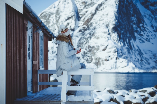 Foto inverno. garota com uma xícara no fundo de rorbu nas ilhas lofoten. noruega