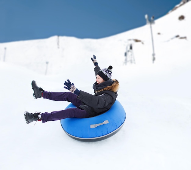 inverno, lazer, esporte e conceito de pessoas - adolescente feliz ou jovem deslizando no tubo de neve sobre o fundo da montanha