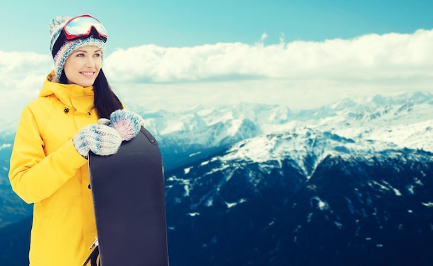 inverno, lazer, esporte e conceito de pessoas - jovem feliz em óculos de esqui com snowboard sobre fundo de montanha nevada