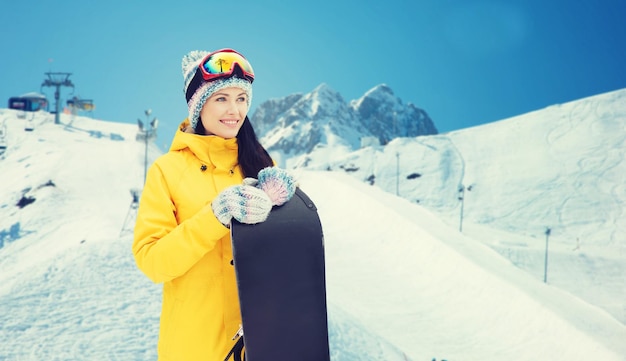 inverno, lazer, esporte e conceito de pessoas - jovem feliz em óculos de esqui com snowboard sobre fundo de neve e montanha