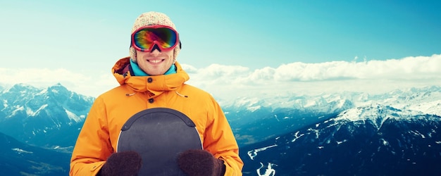 inverno, lazer, esporte e conceito de pessoas - jovem feliz em óculos de esqui sobre fundo de montanha nevada