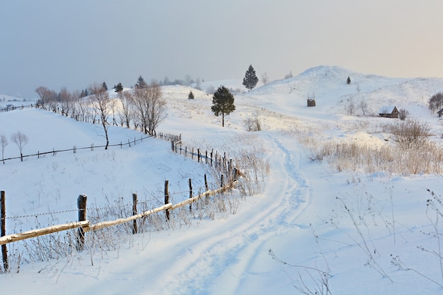 Inverno nas montanhas Colinas de montanhas cobertas de neve A estrada nevada vai para longe perto da cerca