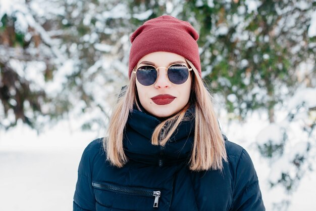 Inverno, Natal, emoções, pessoas, estilo de vida e conceito de beleza - retrato ao ar livre da garota de Natal. Mulher de inverno soprando de neve em um parque. Flocos De Neve Voadores. Dia ensolarado. Retroiluminado. Bom humor