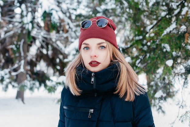 Inverno, Natal, emoções, pessoas, estilo de vida e conceito de beleza - retrato ao ar livre da garota de Natal. Mulher de inverno soprando de neve em um parque. Flocos De Neve Voadores. Dia ensolarado. Retroiluminado. Bom humor