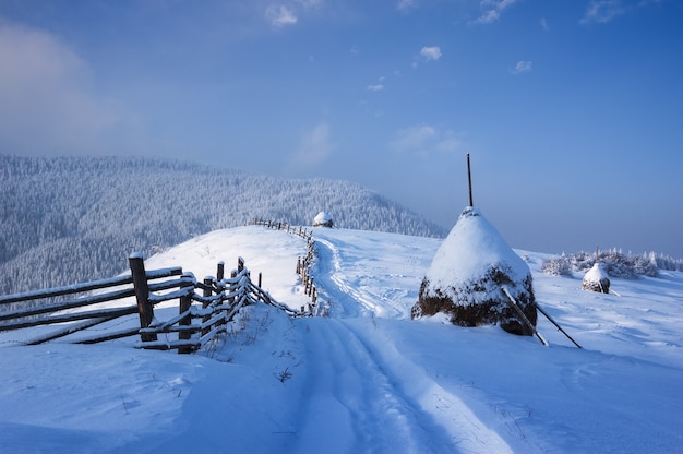 Inverno no campo. Estrada nevada em uma aldeia de montanha. Monte de feno sob a neve