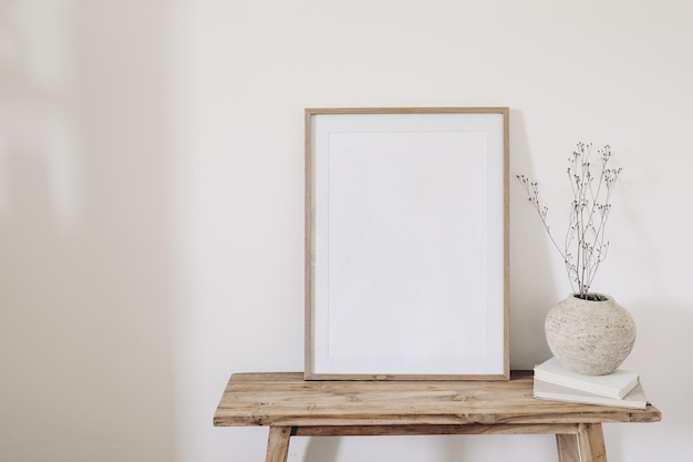 Inverno outono ainda vida Buquê de planta de grama seca em vaso de cerâmica rústico Livros antigos no banco de madeira Maquete de moldura vertical em branco Fundo de parede branca Espaço de cópia vazio nterior escandinavo