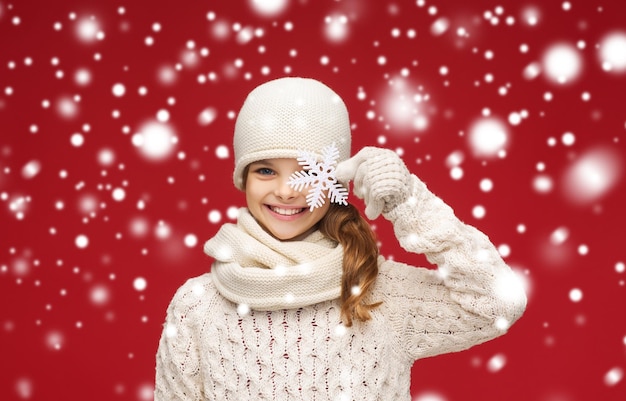 inverno, pessoas, conceito de felicidade - menina sorridente com chapéu, cachecol e luvas com um grande floco de neve