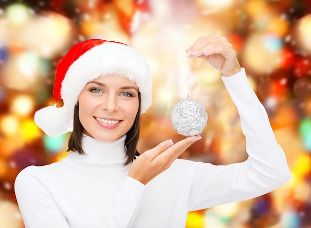 inverno, pessoas, conceito de felicidade - mulher com chapéu de ajudante de papai noel com decoração de árvore de natal sobre fundo de luzes vermelhas