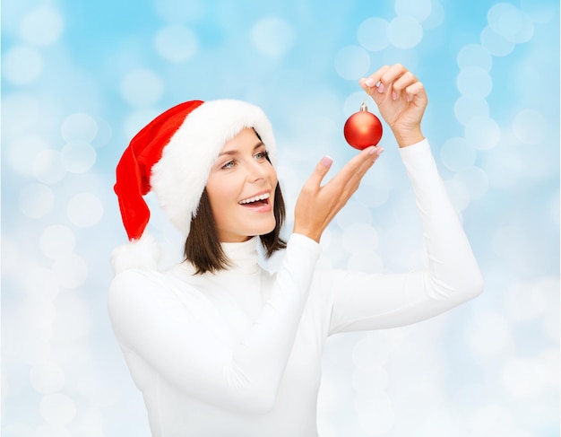 inverno, pessoas, natal e conceito de felicidade - mulher com chapéu de ajudante de papai noel com bola de decoração de árvore de natal sobre fundo de luzes azuis