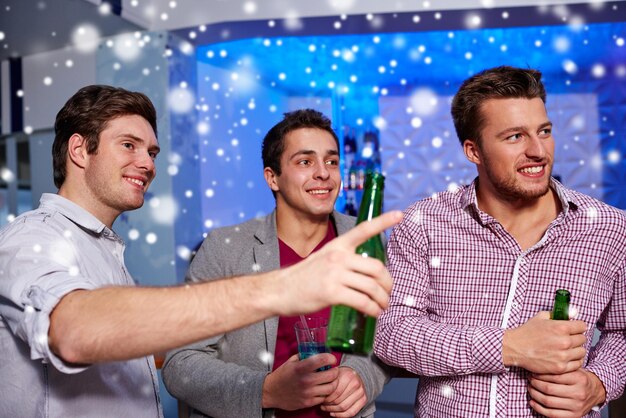 Inverno, vida noturna, amizade, lazer e conceito de pessoas - grupo de amigos do sexo masculino sorridentes com garrafas de cerveja bebendo na boate de despedida de solteiro e efeito de neve