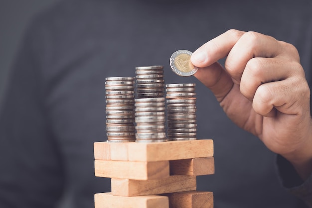 Foto la inversión contiene cierto riesgo idea de un hombre de negocios que ahorra dinero agregando o quitando monedas en la parte superior de una situación de riesgo juego de bloques de madera de la torre riesgos en el concepto comercial o financiero