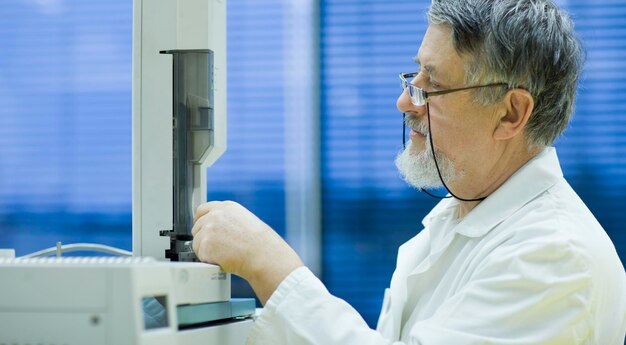 Investigador senior masculino que lleva a cabo investigaciones científicas en un laboratorio utilizando un cromatógrafo de gases DOF superficial imagen en tonos de color