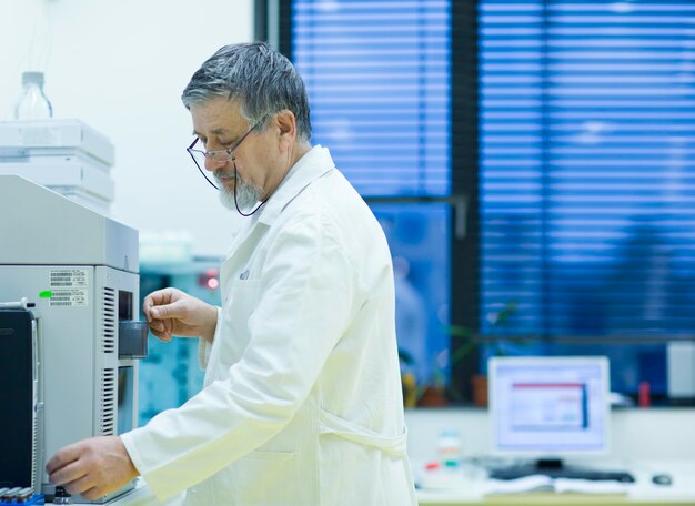 Investigador senior masculino que lleva a cabo investigaciones científicas en un laboratorio utilizando un cromatógrafo de gases DOF superficial imagen en tonos de color