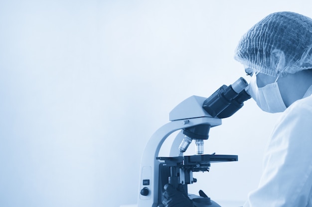 Foto investigadora mirando a través del microscopio en el laboratorio químico moderno haciendo algunas investigaciones