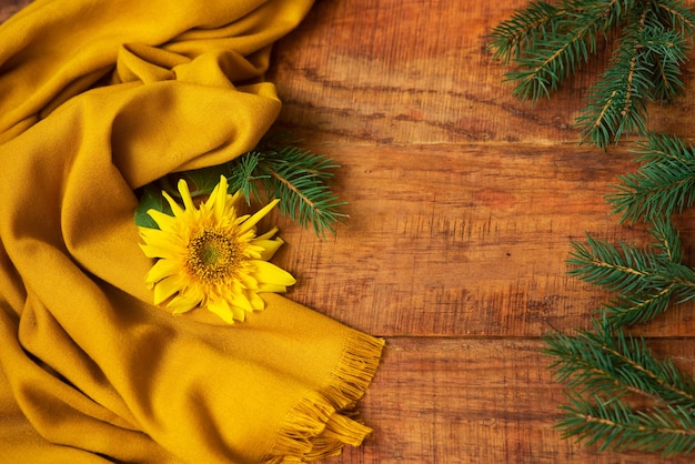 Invierno, ambiente cálido. Una composición con ramas de abeto, pañuelo amarillo y girasol sobre un fondo de madera