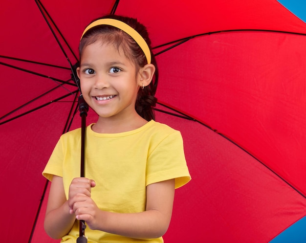 Foto invierno feliz y retrato de un niño con un paraguas abierto y rojo mientras está aislado en un estudio seguridad de la sonrisa y una niña que protege de la lluvia el mal tiempo y el frío para el seguro