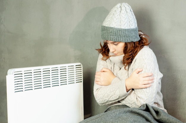 Foto invierno frío en el apartamento una niña calienta sus manos cerca de la energía de la temporada de calefacción de la batería del calentador