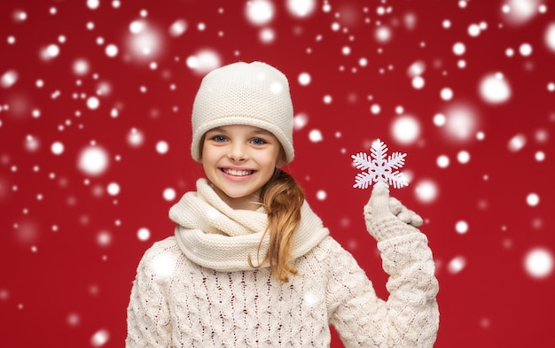 invierno, gente, concepto de felicidad - niña sonriente con sombrero, silenciador y guantes con gran copo de nieve