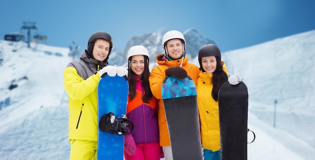 invierno, ocio, deporte extremo, amistad y concepto de personas - amigos felices en cascos con tablas de snowboard sobre esquí alpino y fondo montañoso