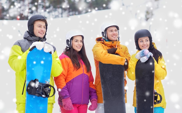 invierno, ocio, deporte extremo, amistad y concepto de personas - amigos felices en cascos con tablas de snowboard