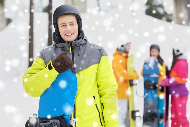 Foto invierno, ocio, deporte extremo, amistad y concepto de personas - joven feliz en casco con snowboard y grupo de amigos