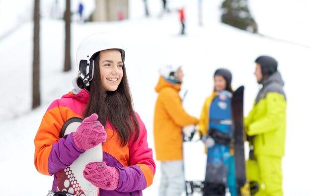 invierno, ocio, deporte extremo, amistad y concepto de personas - mujer joven feliz en casco con snowboard y grupo de amigos