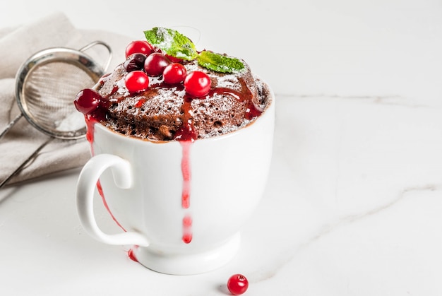 Invierno, otoño desayuno o merienda saludable. La idea de un tratamiento rápido para. Taza de chocolate cupkake en taza de cerámica, con arándanos y salsa, azúcar en polvo. Mesa de mármol blanco,